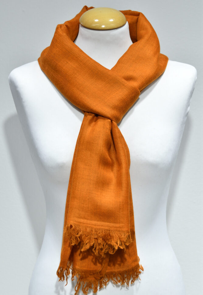 Handvävd pashminasjal i ljus orange på vit provdocka, med fransad kant.